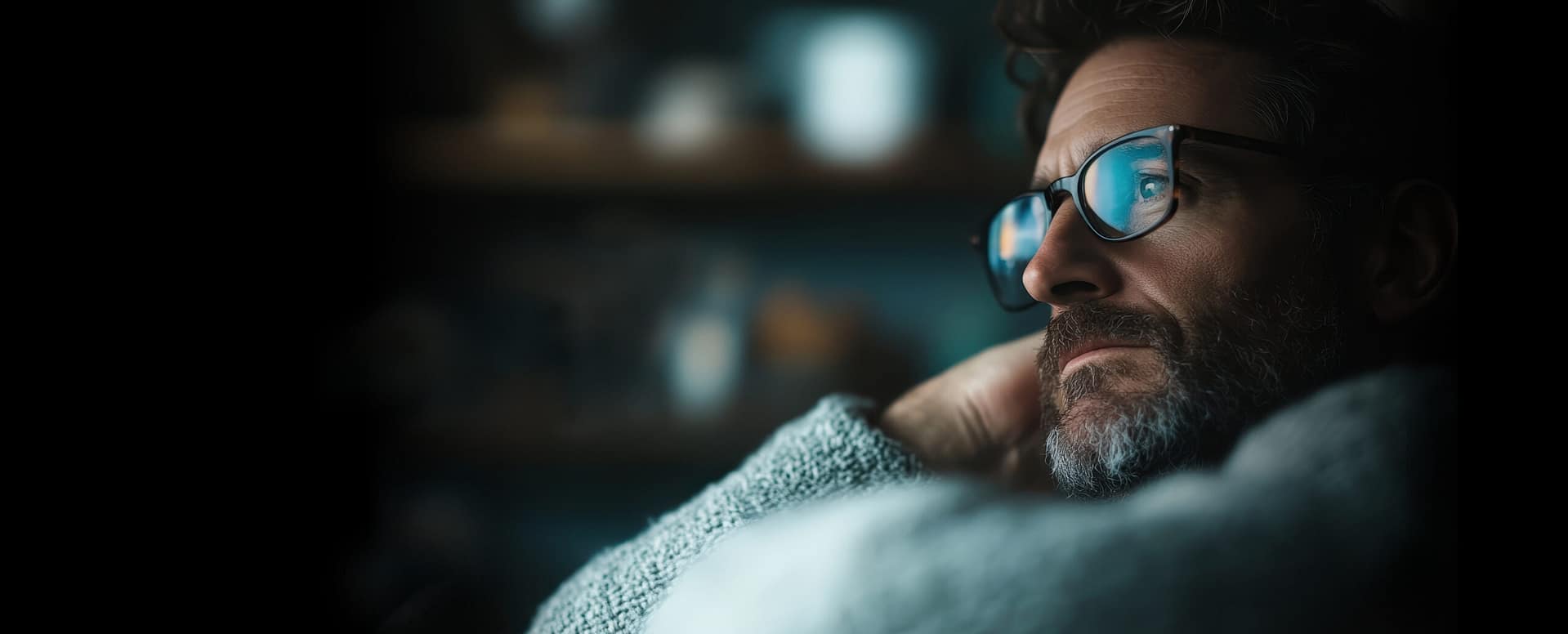 Man in glasses resting and reflecting indoors.